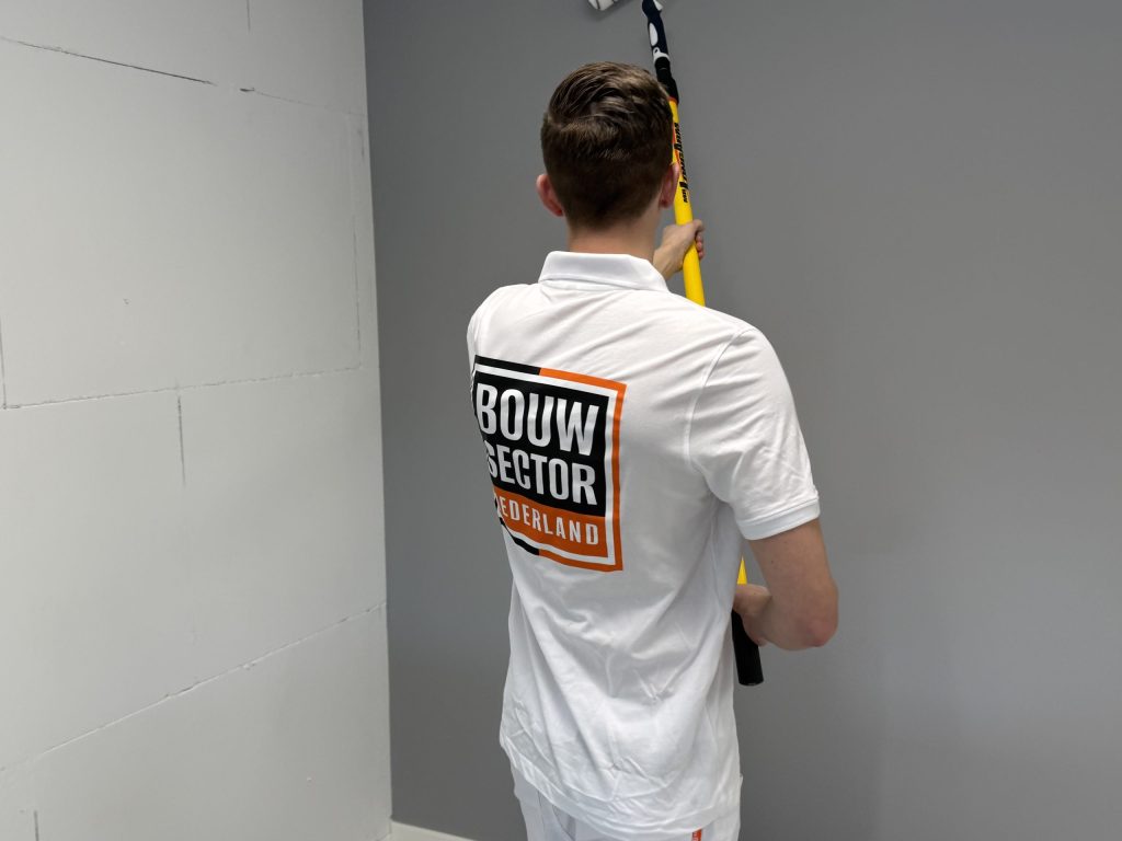 Schilder in wit poloshirt rolt een grijze muur naast een kale wand