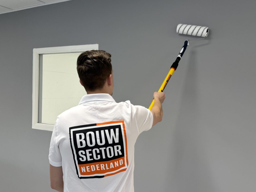 Schilder in bedrijfskleding van Bouwsector Nederland rolt een grijze muur hoog boven het raamkozijn